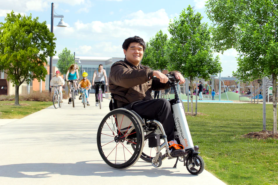 Image of a man using the Companion Plus Power Assist for Manual Wheelchairs - Portable electric power add-on that easily attaches to most manual wheelchairs, providing increased speed and maneuverability.