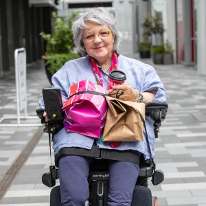 Image of a lady on the LapStacker XD for Permobil Wheelchair - Retractable carry strap system designed for Permobil power wheelchairs, offering versatile and secure carrying options for various items.