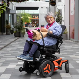 Image of a lady on the LapStacker XD for Permobil Wheelchair - Retractable carry strap system designed for Permobil power wheelchairs, offering versatile and secure carrying options for various items.