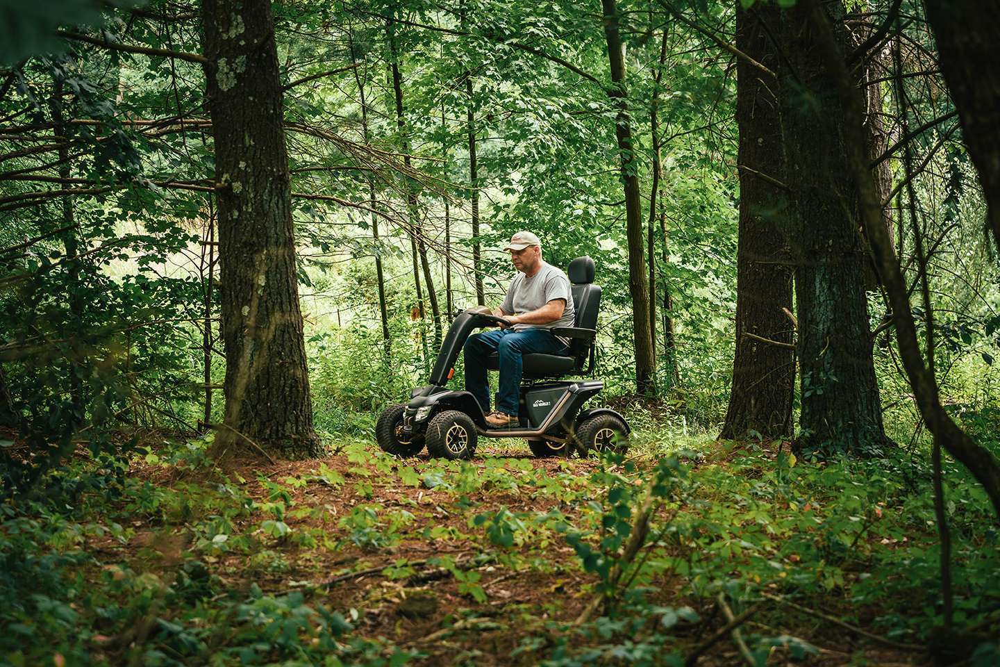 Outdoor image of a man outdoors in the Baja Wrangler 2 Powerchair - All-terrain, electric wheelchair designed for outdoor adventures, featuring large knobby tires, suspension, and waterproof components.