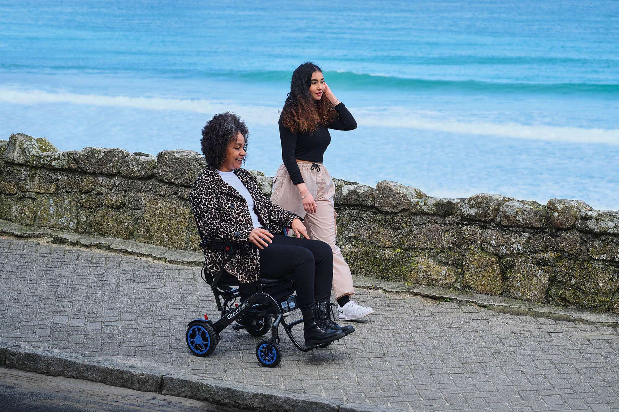 Image of the woman riding alongside a lake in her Quickie Q50 R Carbon Wheelchair - Lightweight, high-performance rigid wheelchair with a carbon fiber frame, designed for increased maneuverability and racing applications.