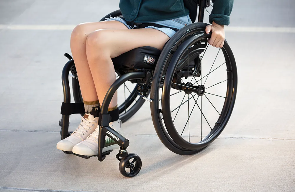 Front left view of girl on the Quickie Nitrum Wheelchair - Lightweight, agile manual wheelchair with a sleek design, ideal for active individuals seeking independence and maneuverability.