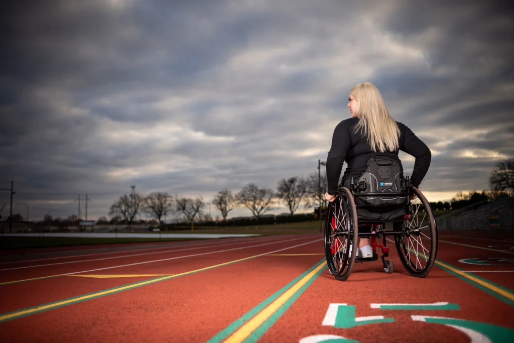 Image of a woman on a track using the Comfort Company Acta-Back Wheelchair Backrest - Customizable, moldable wheelchair backrest featuring aluminum stays for support, viscoelastic foam for comfort, and adjustable hardware for personalized fit.