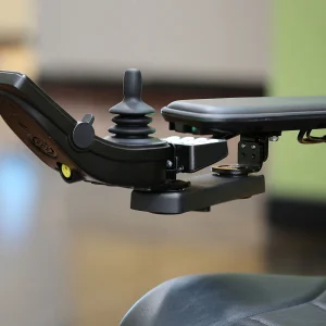 Side view of the Retractable Joystick Mount on wheelchair. A sleek, metal joystick mount attached to a wheelchair armrest. The joystick can be easily swung outwards or retracted sideways for improved accessibility.