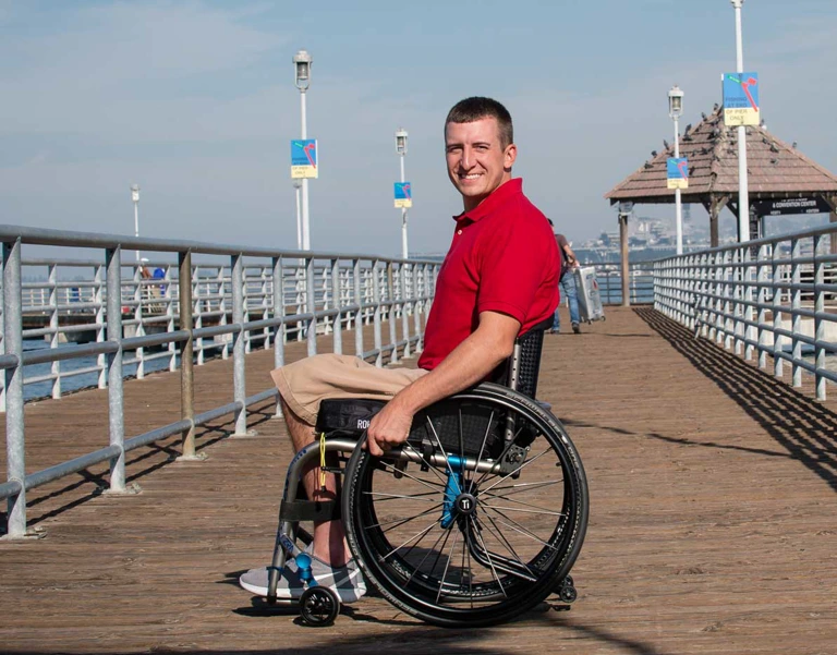 Image of a man using the ROHO® AGILITY® ACTIVE CARBON Min & Mid Contour Back Support - Lightweight, adjustable wheelchair backrest with carbon fiber construction and air cells for improved posture, pressure relief, and ventilation.