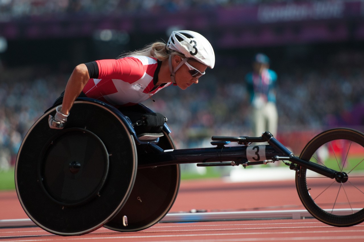 Image of a young woman competing in Competitive Wheelchair Racer Pushing Wheelchair - Athlete propelling specialized racing wheelchair with intense focus and determination.