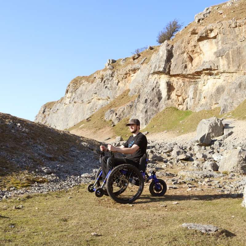 Image of a man outdoors on his Etrike Outdoor Wheelchair - Three-wheeled, all-terrain wheelchair designed for stability and exploration on various outdoor surfaces.